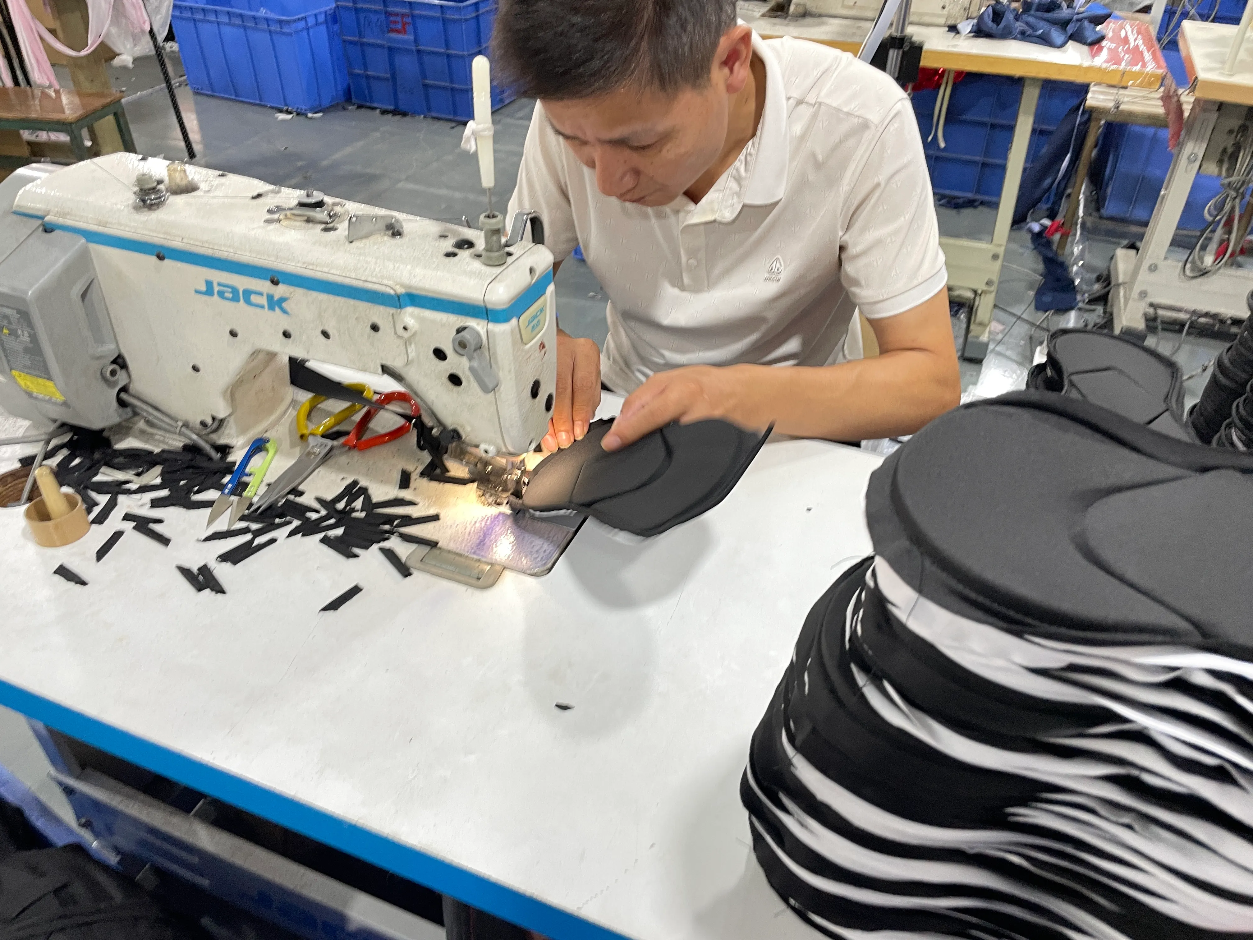 Worker sewing a black protective panel beside a stack of shaped panels.