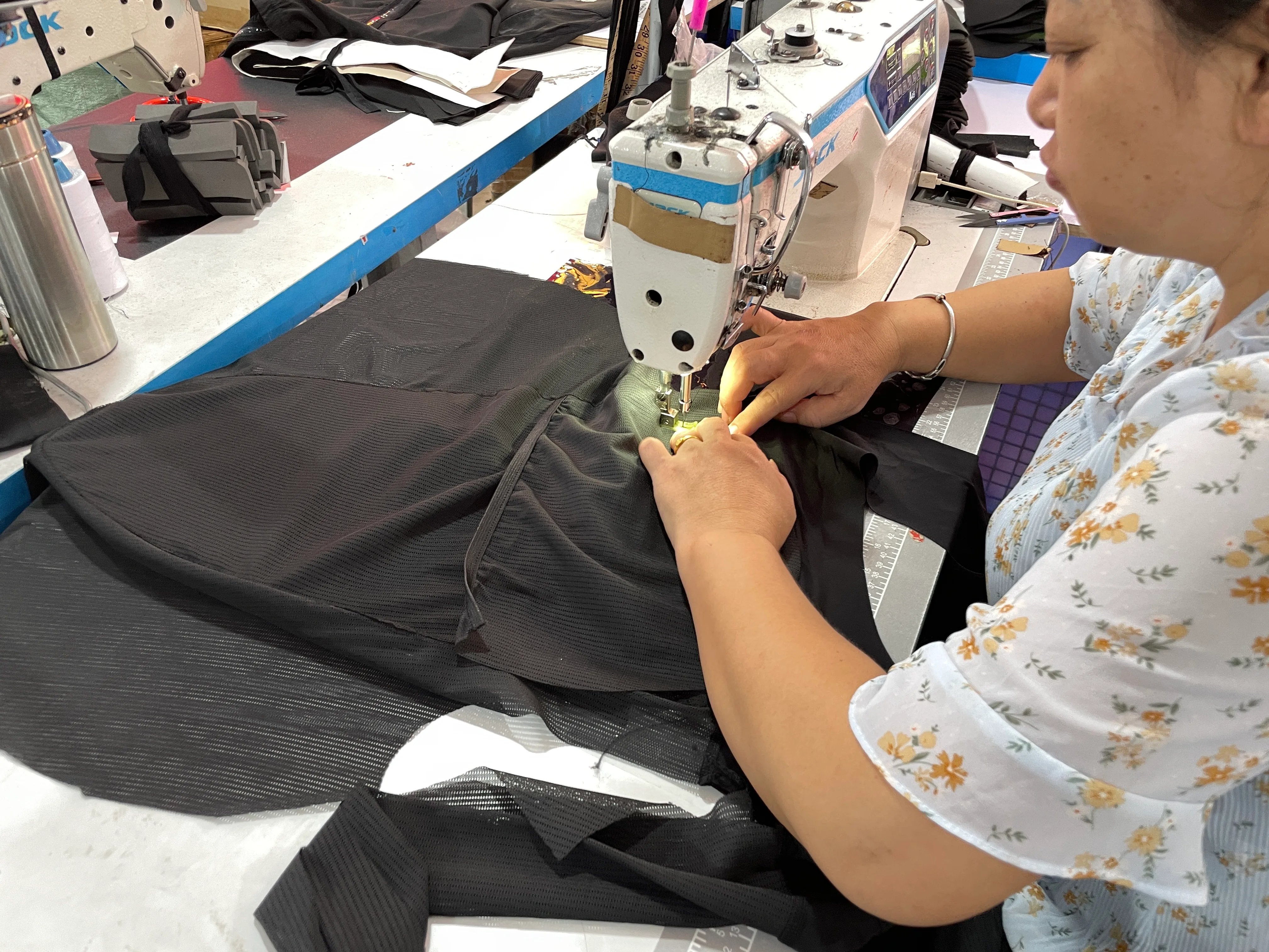 Factory worker stitching a black sports protective garment at an industrial sewing machine